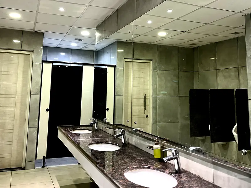 Commercial washroom with a stone vanity, row of basins and toilet cubicles