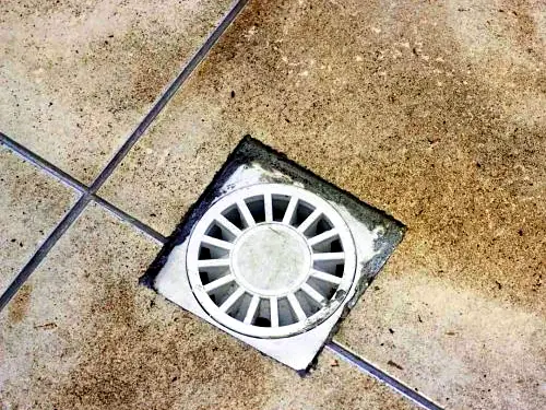 Round floor waste grate set into stained floor tiles