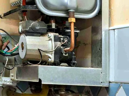 Inside a gas hot water unit showing the gas valve, burner assembly and copper pipework
