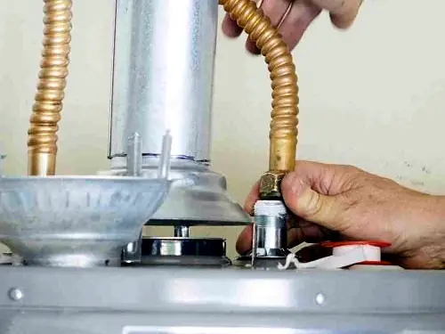 Hands tightening a flexible gas connection on top of a hot water system