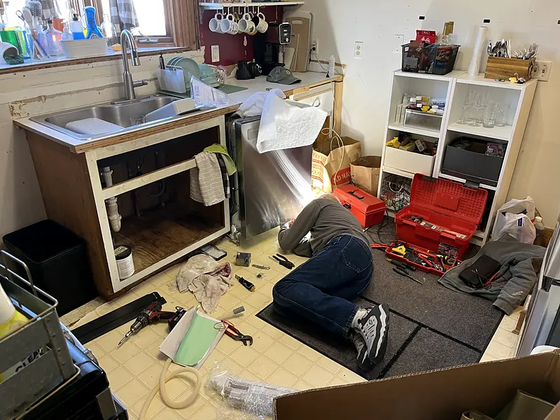 Tradesperson working under a kitchen sink with tools spread across the floor
