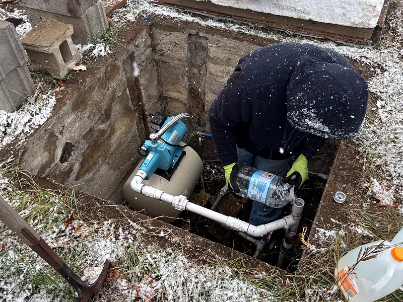 Worker connecting a water pump and white pipework inside an in-ground pit