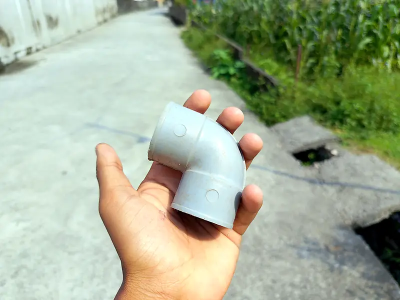 Hand holding a grey PVC elbow pipe fitting
