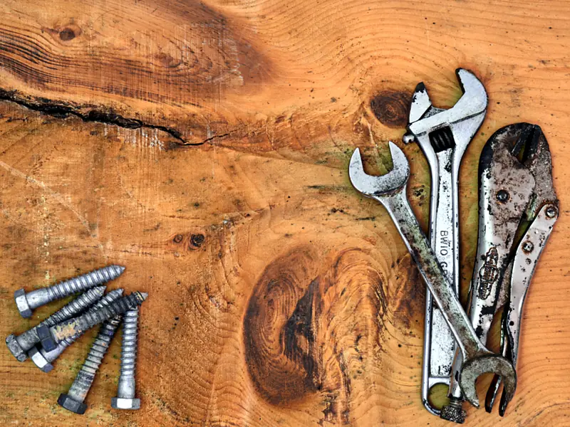 Adjustable wrenches, pliers and bolts laid out on a timber surface